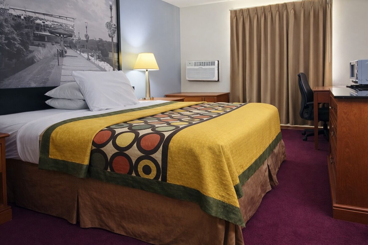 Una habitación de hotel con una cama, un escritorio, una silla, una lámpara y un cuadro en la pared.