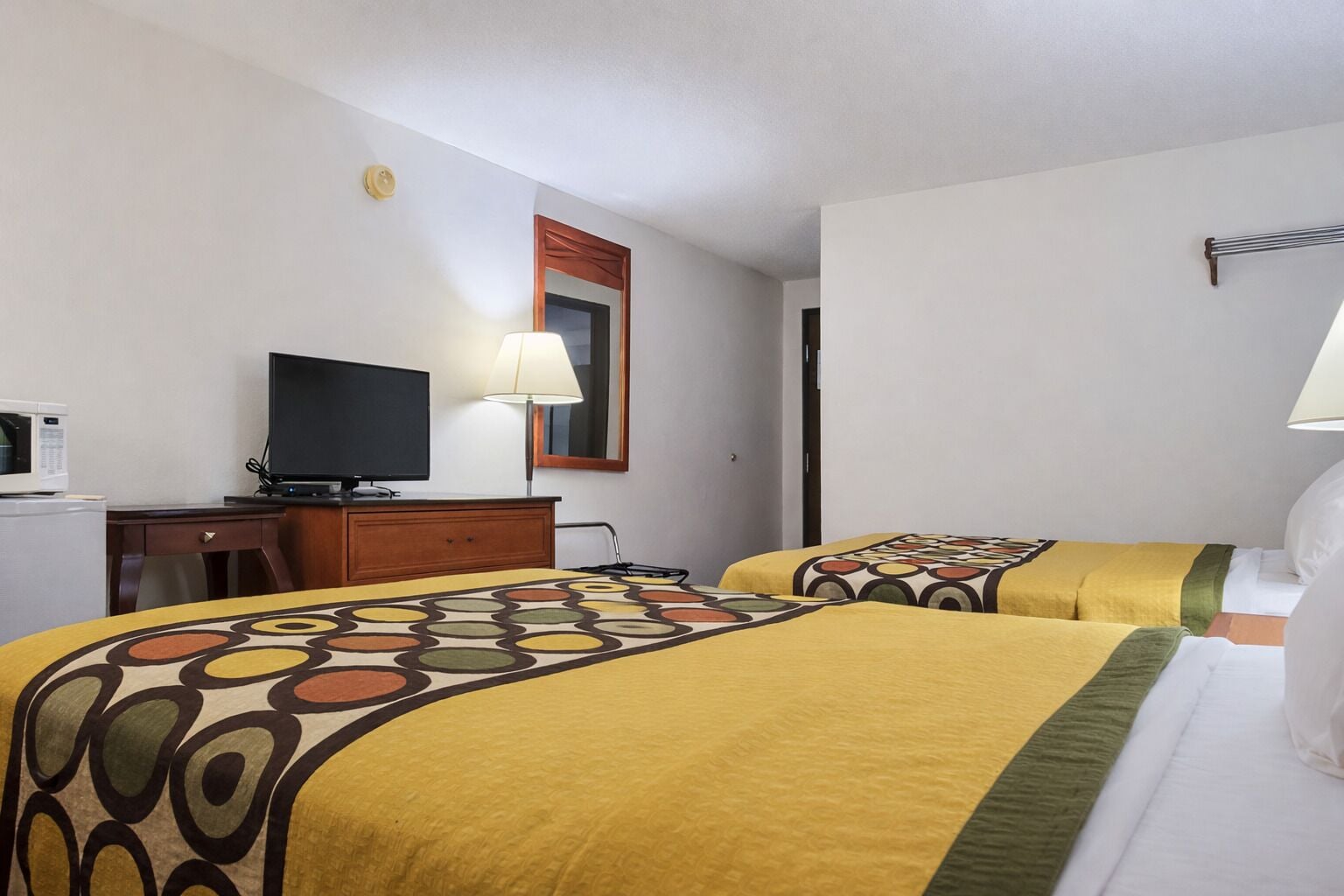 A hotel room with two beds, a desk with a television, a microwave, and a lamp.
