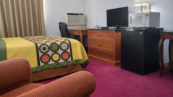 Ein Hotelzimmer mit einem Bett, einem Schreibtisch mit Computer, einem Kühlschrank, einer Klimaanlage und einer Lampe.