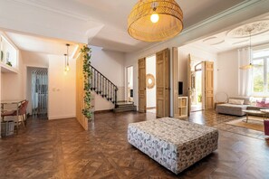 Un vaste espace de vie agrémenté d’un parquet à motifs en chevrons, d’un grand luminaire en fibres tressées et d’un escalier doté d’une rampe en bois.
