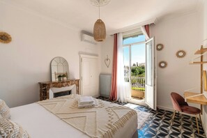 Quarto com cama, penteadeira, espelho, janela com cortinas e vista para o exterior.