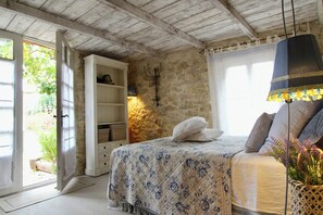 A bedroom with a bed, a wardrobe, a stone wall, and a hanging lamp. - Romantic apartment in historic Provence house (Roquefort-les-Pins)