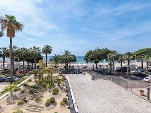 A coastal view with a parking area, palm trees, and a beach in the background. - 2-Br Bourgeois Apartment – Croisette & Sea View (Cannes)