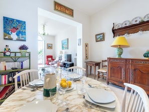A dining area with a table set for four, a bookshelf, a television, and a wooden cabinet with decorative plates. - 2-Br Bourgeois Apartment – Croisette & Sea View (Cannes)
