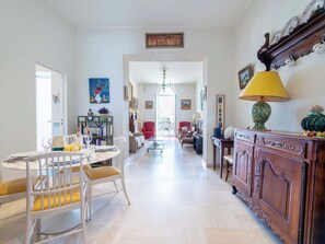 A spacious living area with a dining table, chairs, a red armchair, a wooden cabinet, and a chandelier. - 2-Br Bourgeois Apartment – Croisette & Sea View (Cannes)