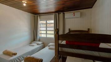 Una stanza con due letti singoli, un letto a castello in legno, una finestra con tende e un condizionatore d'aria.