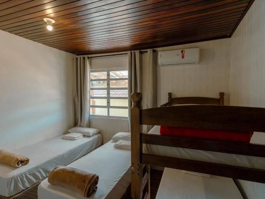 Una stanza con due letti singoli, un letto a castello in legno, una finestra con tende e un condizionatore d'aria.