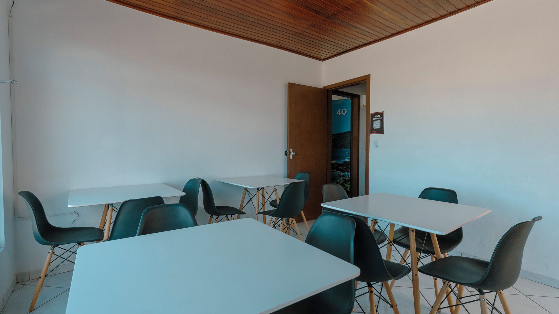 Una stanza con tavoli e sedie bianche, soffitto in legno e una porta con il simbolo del numero.