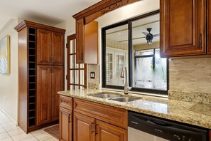 A kitchen with wooden cabinets, granite countertops, a double sink, and a dishwasher. - Sarasota Pool Home Near UTC & Beaches + Hot Tub + Lakefront Patio (Sarasota)
