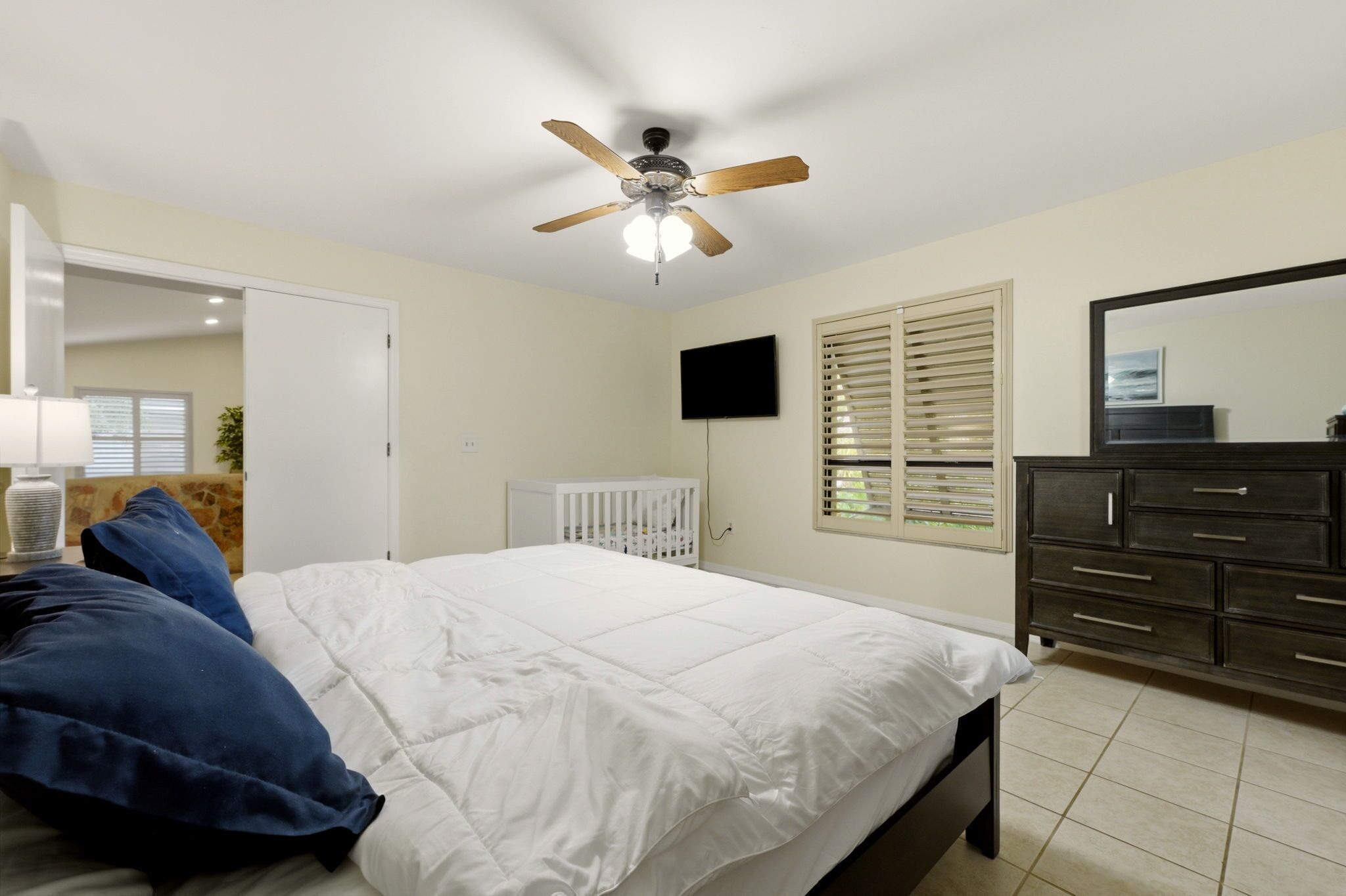 Une chambre à coucher avec un lit, un ventilateur de plafond, une télévision, une commode et un berceau.