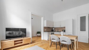 Een modern appartement met een televisie, eettafel, stoelen, keuken en een visgraatvloer.
