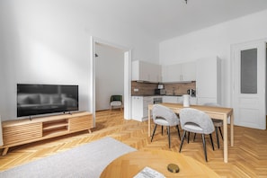 A modern apartment with a TV, dining table, chairs, kitchen, and a herringbone-patterned floor. - Blueground | Alsergrund, view, nr Votivkirche (Vienna)