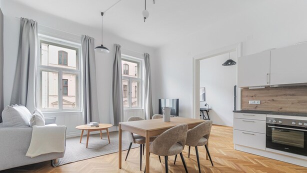 Een moderne woonkamer met een bank, een eettafel met stoelen, een televisie en een keukenhoek met een fornuis.