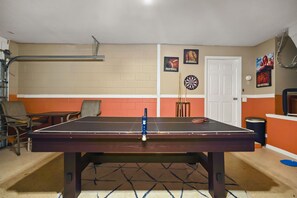 Uma mesa de bilhar em um espaço com uma porta, um alvo de dardos e decoração temática de esportes.