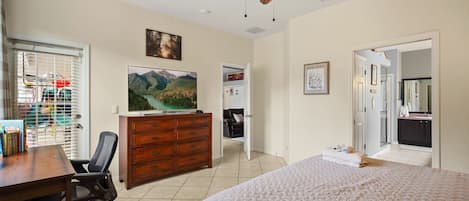 A bedroom with a bed, a desk, a dresser, a ceiling fan, and a TV.