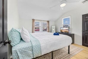 A bedroom with a bed, a desk, a television, and a window with a view of the outside. - Ventnor Home | BBQ + Fenced Yard | Beach Gear Incl (Ventnor City)