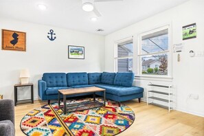 Una sala de estar con un sofá seccional azul, una mesa de centro, una alfombra colorida, una lámpara y un cuadro en la pared.