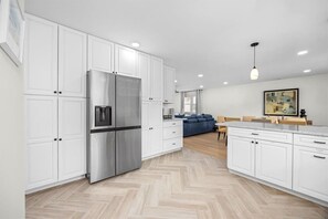 A modern kitchen with white cabinetry, a stainless steel refrigerator, and a herringbone-patterned floor. - Modern Ventnor Retreat | Sleeps 8 | Backyard (Ventnor City)