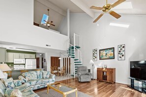 A spacious living area with a sofa, armchair, and TV stand. A staircase leads to an upper level with a ceiling fan. - Bright Condo w/ Loft for 8! Bay Tree 24B (Little River)
