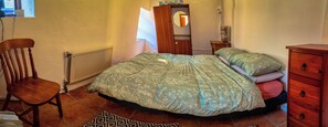 A bedroom with a bed, a chair, a dresser, a radiator, and a mirror.