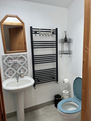 A bathroom with a white sink, a mirror, a black towel rack, a toilet, and a patterned tile backsplash.
