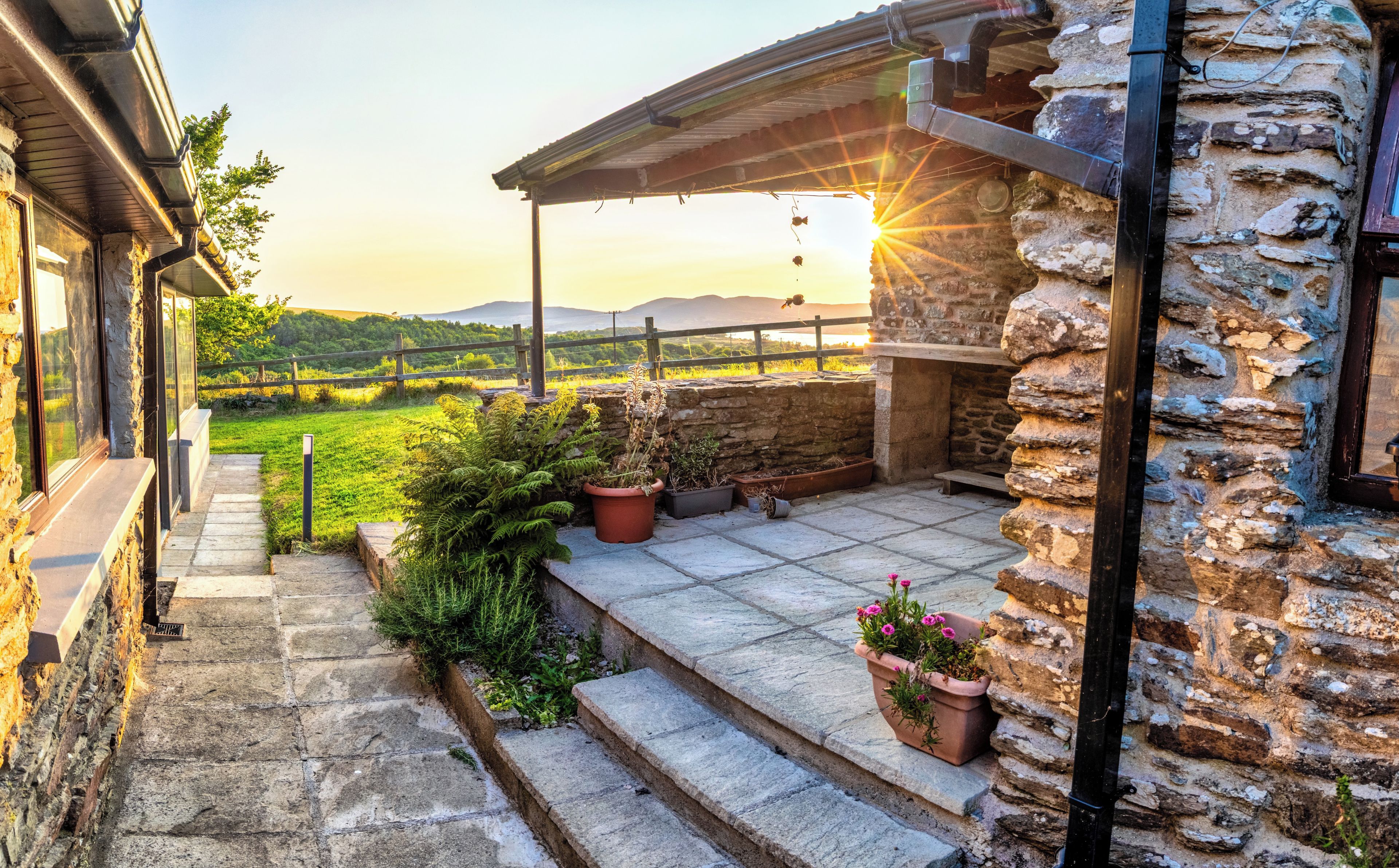 A stone staircase leading to a balcony with a view of a green landscape and mountains in the distance.
