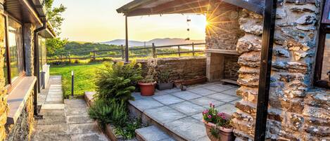A stone staircase leading to a balcony with a view of a green landscape and mountains in the distance.