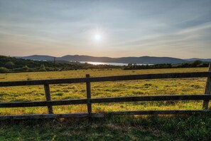 A grassy field with a wooden fence in the foreground and a body of water with mountains in the background.
