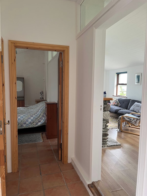 A room with a bed, a wooden door, a stone wall, and a view of a living area with a sofa and a window.