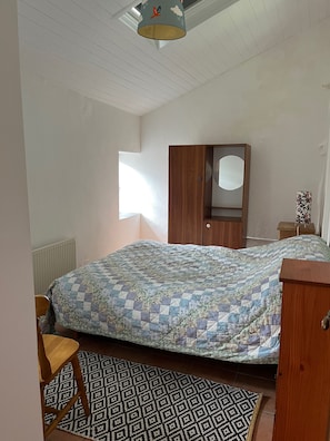 A bedroom with a bed, a wooden wardrobe, a window, and a patterned rug.