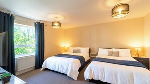 Een hotelkamer met twee bedden, een bureau, een televisie en een raam met gordijnen.