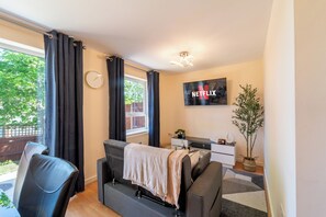 Ein modernes Wohnzimmer mit einer Couch, einem an der Wand montierten Fernseher, einer Uhr und einer Topfpflanze.