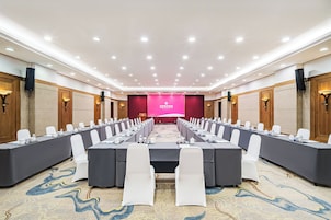 A conference room with long tables, white chairs, and a stage with a pink backdrop.