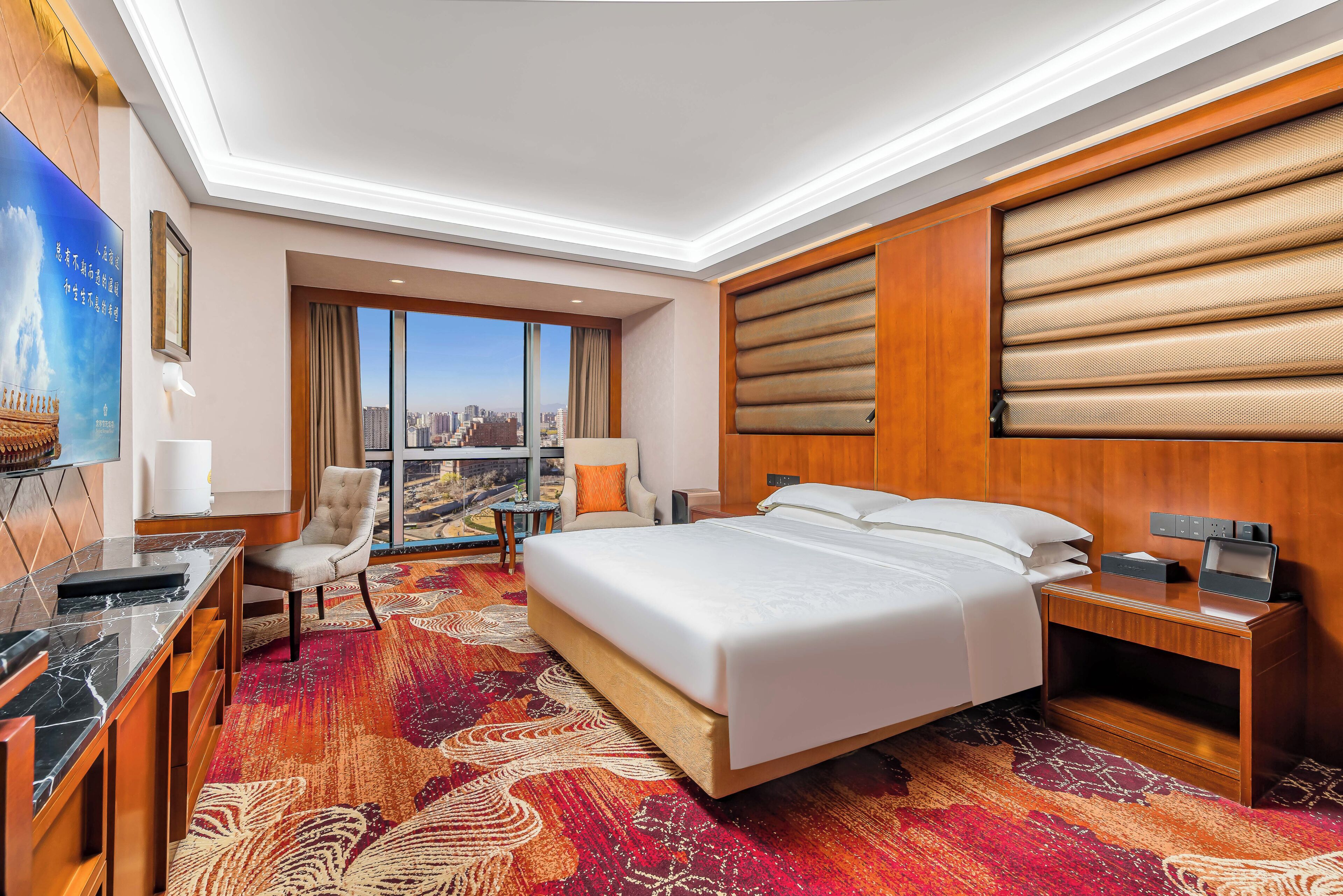 A hotel room with a large bed, a desk with a chair, a small table, and a view of the city.
