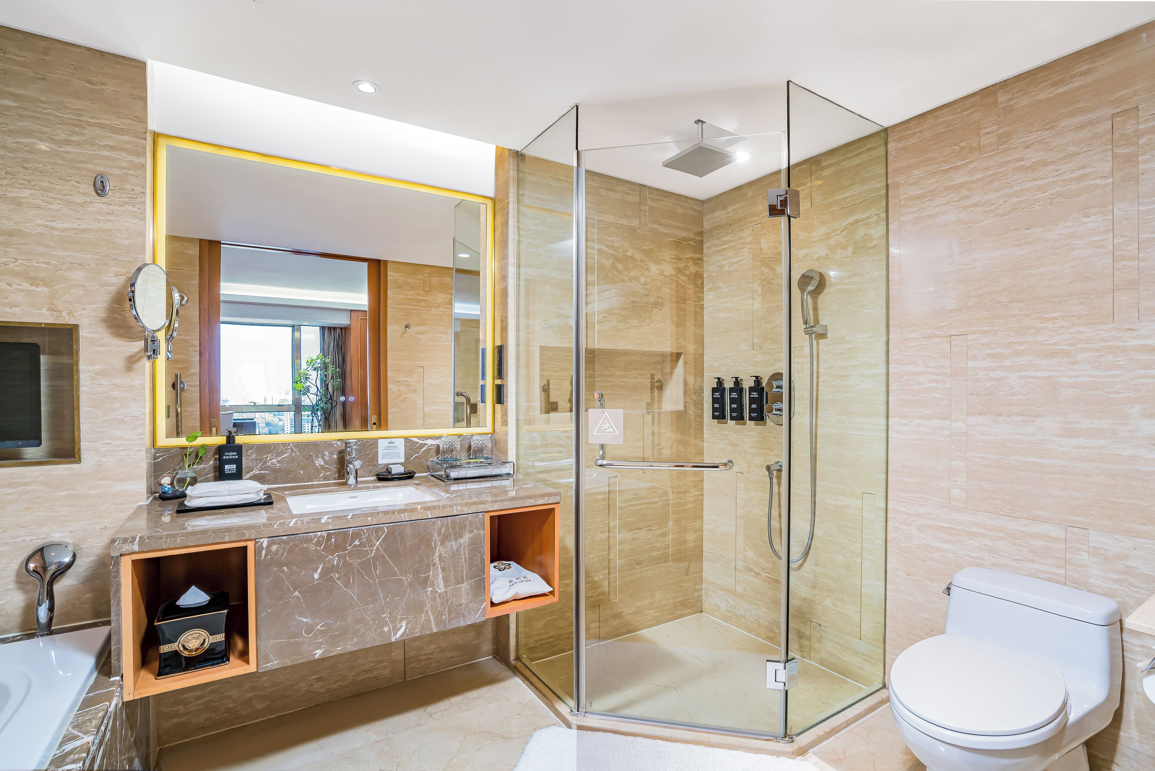 Un baño moderno con ducha envuelta en vidrio, tocador de mármol, espejo grande y un inodoro.
