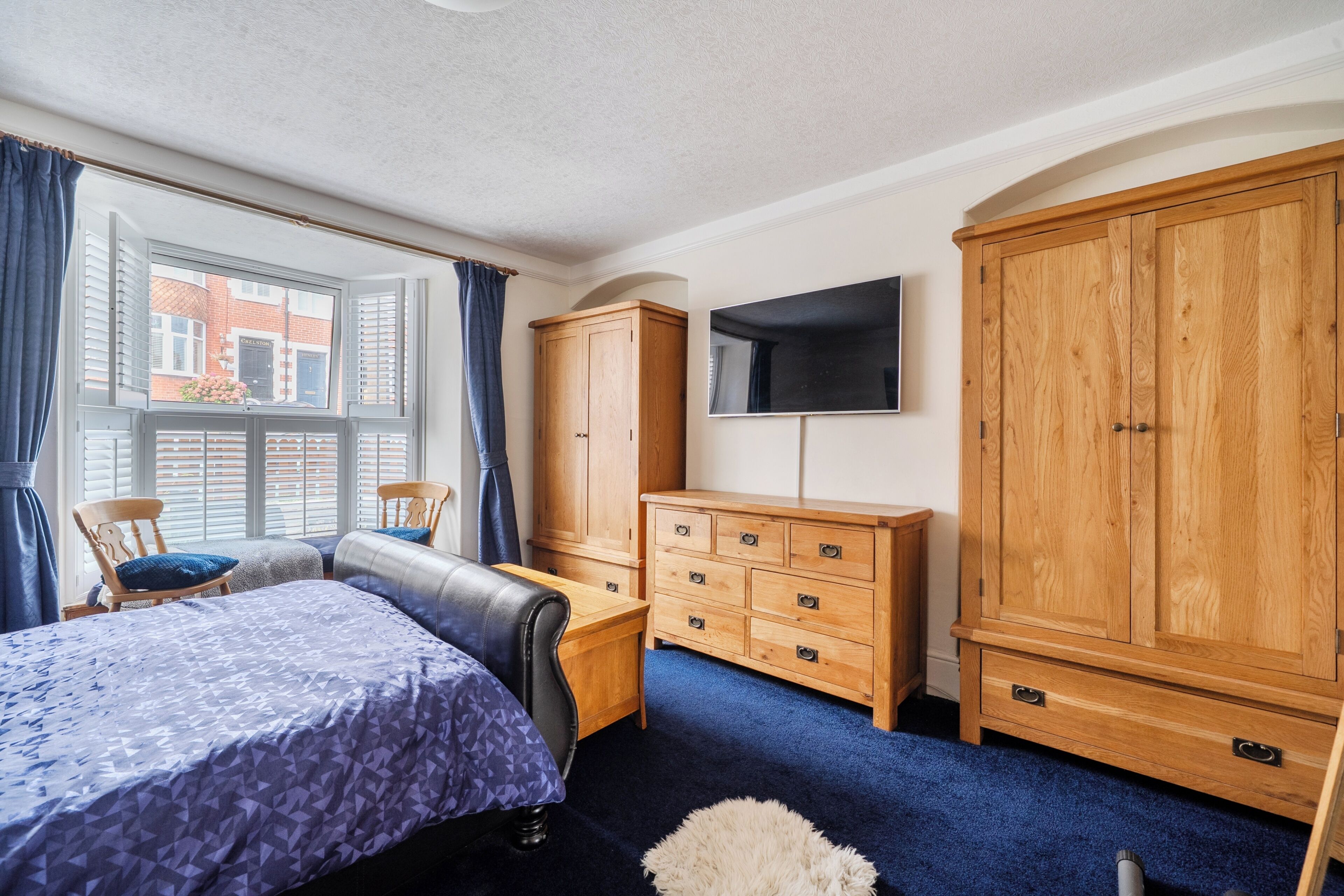 Een slaapkamer met een bed, een houten garderobe, een televisie en een raam met luiken.