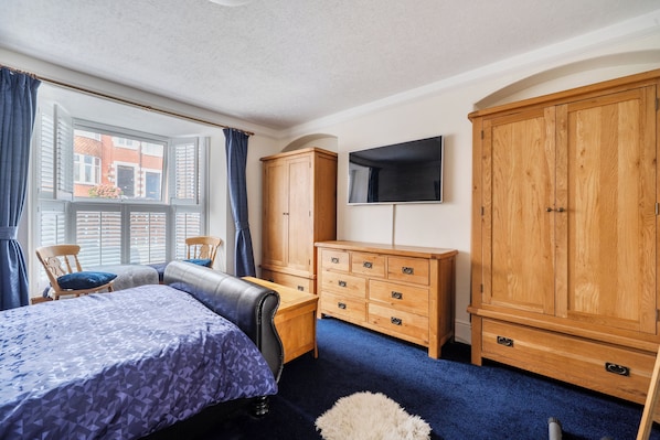A bedroom with a bed, a wooden wardrobe, a television, and a window with shutters. - 1 Bed - Sleeps 4 - Parking - Pets - Town Centre (Wadebridge)