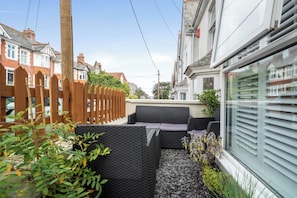 A narrow urban street with traditional houses, a wooden fence, and a seating area with wicker furniture. - 1 Bed - Sleeps 4 - Parking - Pets - Town Centre (Wadebridge)