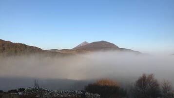 A mountainous landscape with a prominent peak, a stone wall, and a foggy valley.