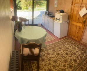 Una cocina compacta con microondas y estufa, una mesa de comedor con una silla, y una alfombra estampada.