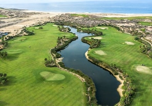 Ein Golfplatz mit Wasserhindernissen, Sandbunkern und einer Küstenlandschaft im Hintergrund.