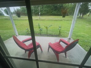 A screened porch with two red chairs and a table, overlooking a grassy yard with trees and a fence. - Bluegrass basecamp 2 bedroom home prime location central to all RRG activities (Rogers)