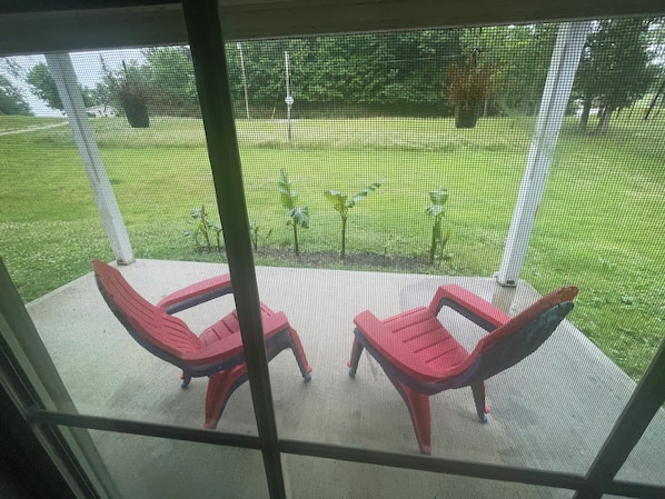 A screened porch with two red chairs and a table, overlooking a grassy yard with trees and a fence. - Bluegrass basecamp 2 bedroom home prime location central to all RRG activities (Rogers)