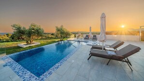 Ein Pool auf dem Dach mit Liegestühlen und Sonnenschirmen, umgeben von Bäumen und Blick auf den Sonnenuntergang.