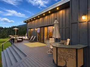 A modern outdoor deck with seating, a glass table, and a pergola.