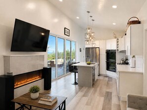 A modern kitchen with a fireplace, a dining area, and a large window overlooking a deck.