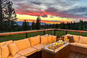 A deck with a fire pit and outdoor seating, overlooking a forested landscape.