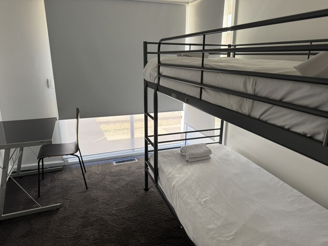 A bunk bed with a desk and chair, a window, and a carpeted floor.