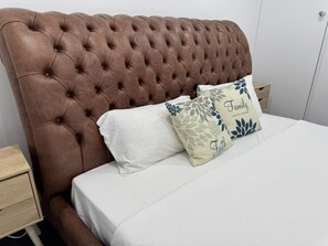 Un dormitorio con un cabecero capitonado, una colcha blanca y dos almohadas decorativas.
