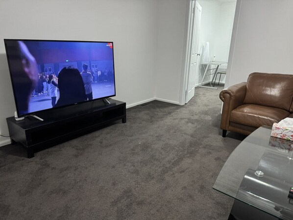 Una sala de estar con una televisión de pantalla plana sobre un mueble, un sofá de cuero marrón y una mesa de centro de vidrio.